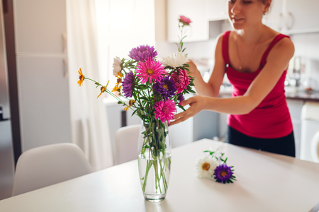 Woman puts pink flowers in vase. Young housewife taking care of coziness in kitchen. Modern kitchen design. White and silver kitchenの写真素材