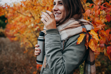 Young woman holds a bottle and drinks tea in autumn forestの写真素材