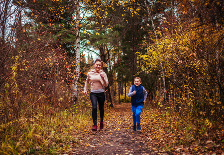 Little boy and his sportive sister running in autumn forestの写真素材