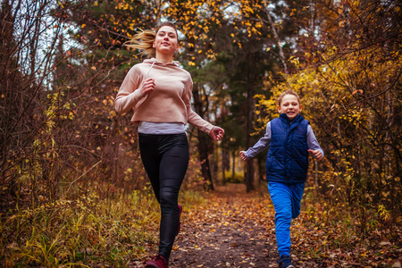 Little boy and his sportive sister running in autumn forestの写真素材