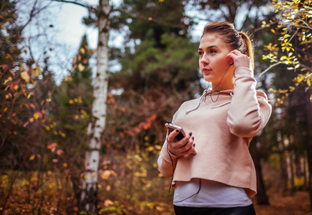 Woman runner puts her headphones on to listen to the music while running in the forestの写真素材
