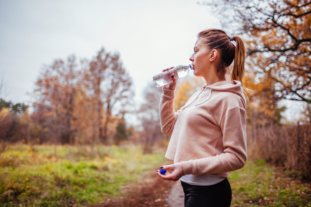 Woman runner having rest and drinks water in autumn forestの写真素材