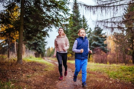 Little boy and his sportive sister running in autumn forestの写真素材