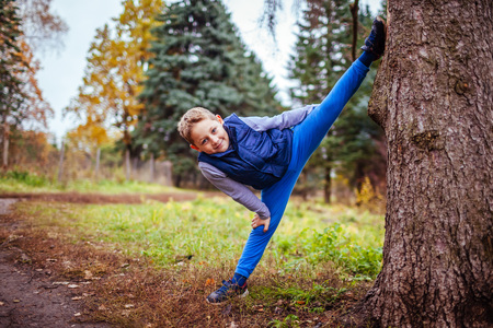 Little boy shows splits standing by the tree in autumn forestの写真素材