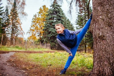 Little boy shows splits standing by the tree in autumn forestの写真素材