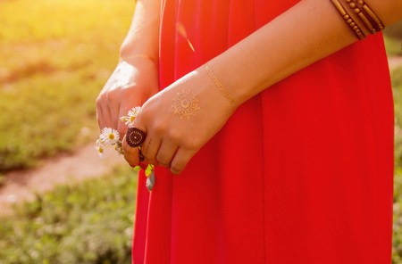 Golden mehendi tattoo on woman's hands in red dress outsideの写真素材