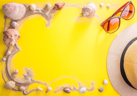 Vacation concept. Sand, seashells, sunglasses and hat on yellow backgroundの写真素材