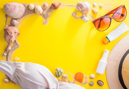 Vacation concept. Sand, seashells, cosmetics and accessories on yellow backgroundの写真素材
