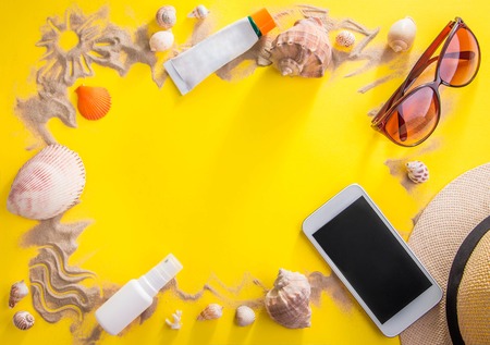 Vacation concept. Sand, seashells, sunglasses, suncream, smartphone and hat yellow background. Spaceの写真素材