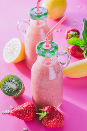 Fruity smoothie in glass bottles with ingredients on pink backgroundの写真素材