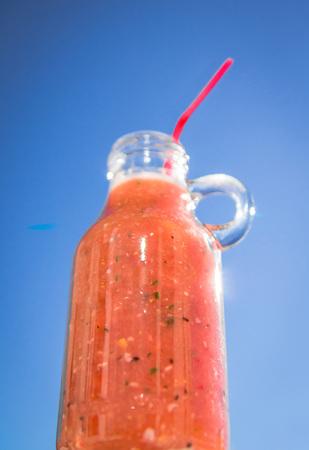 Woman holds a bottle of smoothie against the blue skyの写真素材