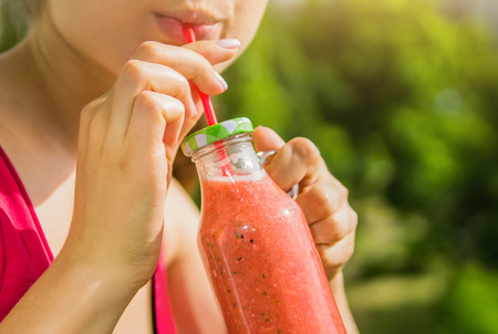 Woman drinks fruity smoothie in glass bottle with straw outsideの写真素材