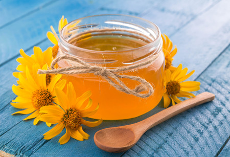 Honey in a glass jar with stick surrounded with yellow flowers on blue wooden tableの写真素材