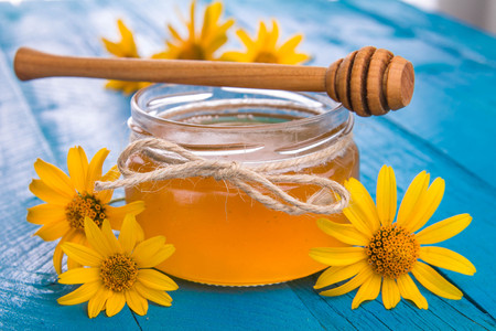 Honey in a glass jar with stick surrounded with yellow flowers on blue wooden tableの写真素材