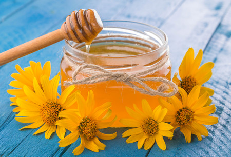Honey in a glass jar with stick surrounded with yellow flowers on blue wooden tableの写真素材