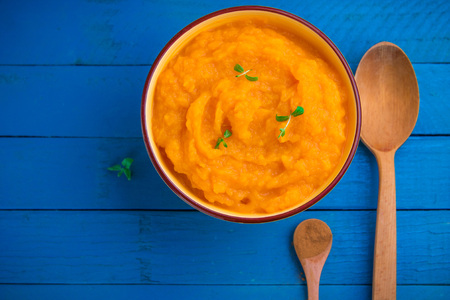 Pumpkin cream soup in bowl with herbs and wooden spoons on blue wooden backgroundの写真素材