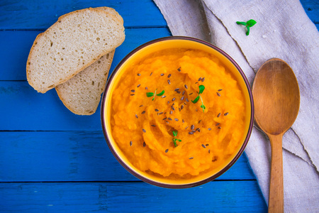 Pumpkin cream soup with herbs and bread in a bowl on blue wooden backgroundの写真素材