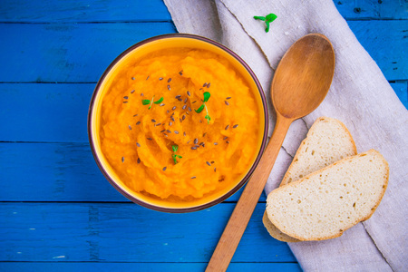 Pumpkin cream soup with herbs and bread in a bowl on blue wooden backgroundの写真素材