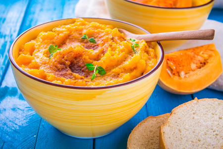 Pumpkin cream soup with mint and bread in a bowl on blue wooden backgroundの写真素材