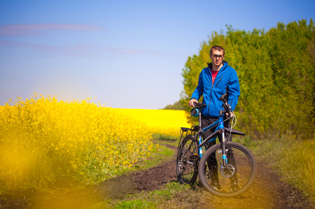 Young bicyclist rides in spring rapeseed field on mountain bikeの写真素材