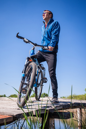 Young bicyclist rides on mountain bike on the bridge across the riverの写真素材