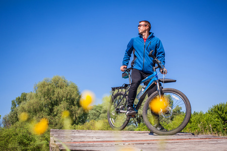 Young bicyclist rides on mountain bike on the bridge across the riverの写真素材