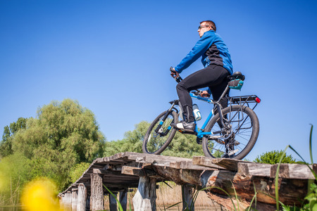 Young bicyclist rides on mountain bike on the bridge across the riverの写真素材
