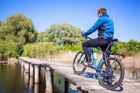 Young bicyclist rides on mountain bike on the bridge across the riverの写真素材
