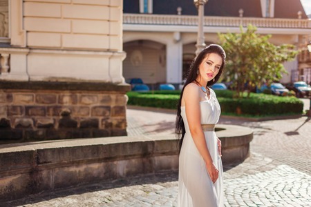 Beautiful woman wearing white wedding dress outdoors in old city. One shoulder dress with accessories and jewellery. Fashion. Stylish makeupの写真素材