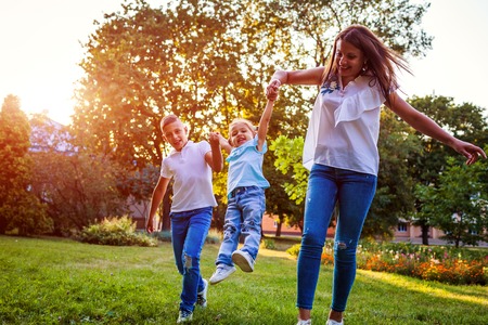 Happy family spending time outdoors playing in park. Mom having fun with two kids boy and girl. Tossing girl up. Family valuesの写真素材
