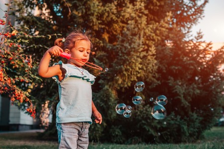 Little toddler girl blowing soap bubbles in summer park. Happy kid playing outdoors. Child having funの写真素材