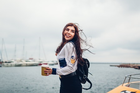 College woman student of Marine academy drinking coffee by sea wearing uniform. Girl walking in seaport of Odesa on pierの写真素材