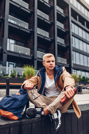 College student with backpack reading book chilling by modern hotel on rainy autumn day. Guy chilling outdoors. Education conceptの写真素材