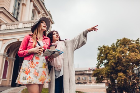 Two women tourists searching for right way using map in Odessa. Happy friends travelers showing direction and laughingの写真素材