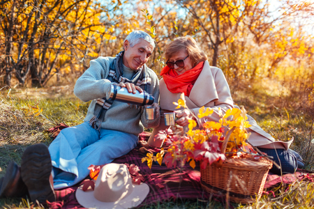 Senior couple having tea in autumn forest. Happy man and woman enjoying picnic and natureの写真素材