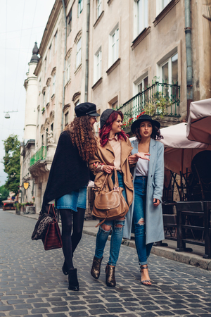 Outdoor shot of three young women walking on city street. Happy girls talking and huggingの写真素材