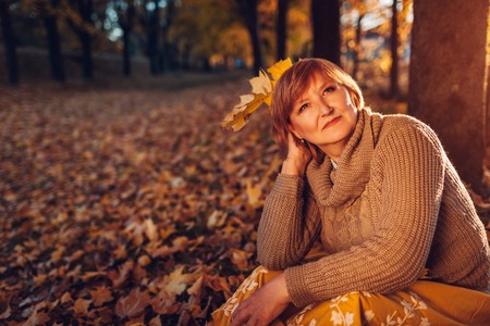 Middle-aged woman holding bouquet of maple leaves. Lady enjoying autumn nature and relaxing sitting...
