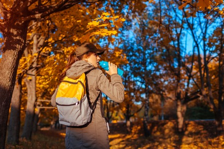 Tourist with backpack walking in autumn forest. Young woman drinking water. Traveller having rest