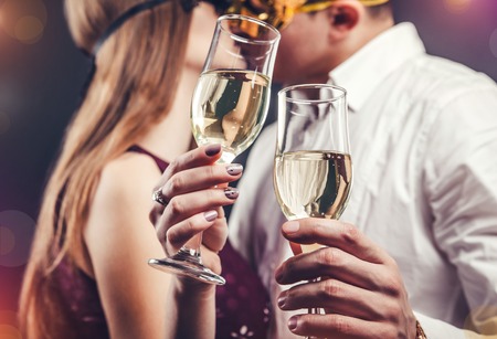 Young couple celebrating New Year's eve drinking champagne on masquerade party and kissingの写真素材