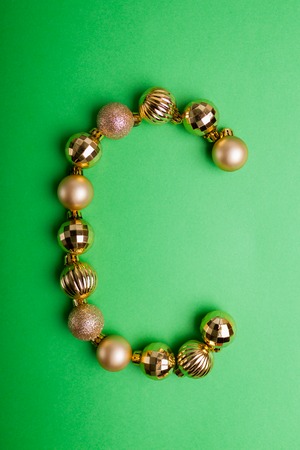 Letter C made of Christmas toys on green background. ABC made of golden ballsの写真素材
