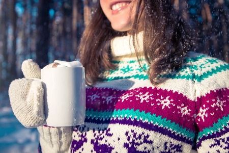 Young woman holds cup of coffee with marshmallow in winter forestの写真素材