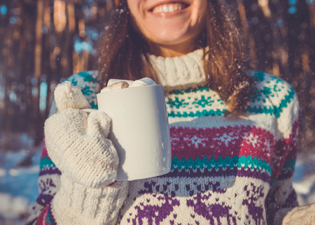 Young woman holds cup of coffee with marshmallow in winter forestの写真素材
