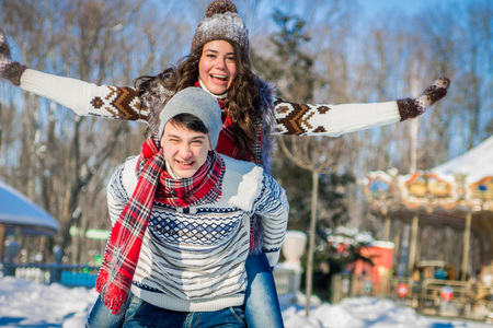 Woman rides on her boyfriend's back in winter park. Man giving girlfriend piggyback