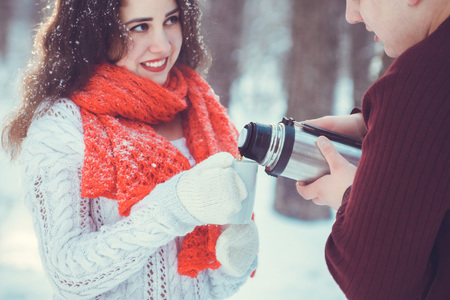 Young couple pours hot tea out of thermos in winter forestの写真素材