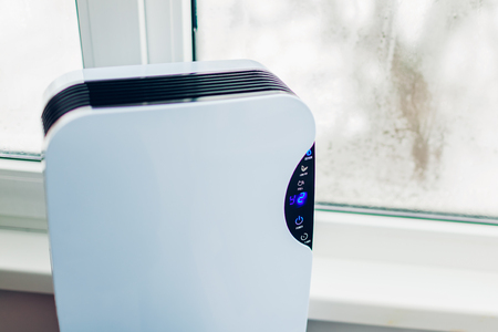 Dehumidifier with touch panel, humidity indicator, uv lamp, air ionizer, water container works by wet window in flat. Close upの写真素材