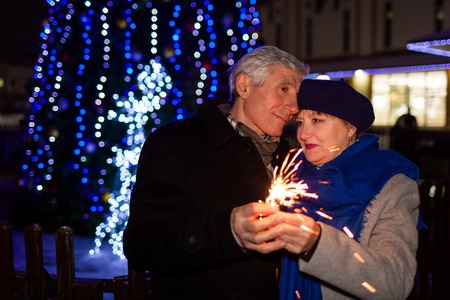 Senior family couple burning sparklers by holiday illumination at night. Christmas and New year conceptの写真素材