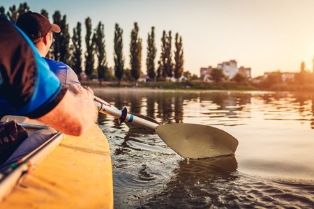 Young men rowing kayak on river at sunset. Couple of friends having fun canoeing in summer. Closeup of paddlesの写真素材