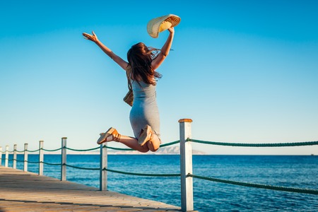 Young woman traveler jumping feeling happy and free on pier by Red seaの写真素材