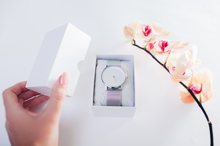 Woman opens a gift box with silver hand watch surrounded with orchid. Present for Valentine's day with flowersの写真素材