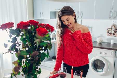 Young woman found bouquet of roses with candle, wine and gift box on kitchen. Happy excited girl. Valentines day surpriseの写真素材